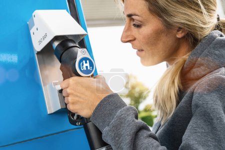 Foto de Mujer sostiene un dispensador de combustible con el logotipo de hidrógeno en la gasolinera para llenar su coche. motor de combustión h2 para la imagen concepto de transporte ecológico libre de emisiones - Imagen libre de derechos
