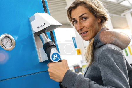 Photo for Woman holds a fuel dispenser with hydrogen logo on gas station to fill up her car. h2 combustion engine for emission free eco friendly transport concept image - Royalty Free Image