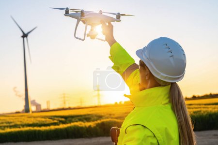 Téléchargez les photos : Exploitant femelle tenant un drone pour inspecter le coucher du soleil de l'éolienne. Image concept d'inspection de drones. parc éolien d'énergie renouvelable en Europe - en image libre de droit