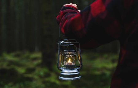 Hiker holding a oil lantern or kerosene lamp and walking in the dark forest