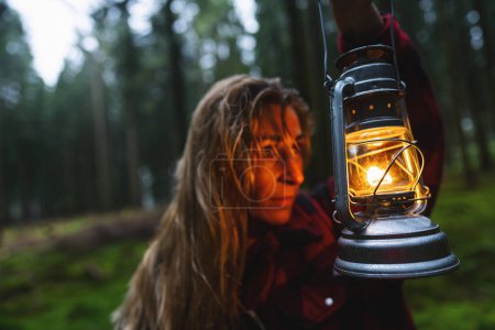 Foto de Senderista femenina con cabello húmedo sosteniendo lámpara de queroseno o lámpara de aceite en el bosque. auténtico primer plano. Imagen del concepto de viaje - Imagen libre de derechos