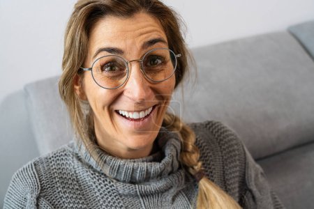 Photo for Pretty girl with pigtail, wearing glasses and gray sweatshirt, laughing. Close-up front portrait indoors with copy space - Royalty Free Image