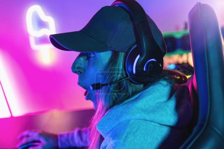 Photo for Astonished female Gamer plays Online Video Game on her Personal Computer. Room Lit by Neon Lights in Retro Arcade Style. Online Cyber e-Sport Internet Championship. - Royalty Free Image