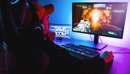Photo for Professional Gamer thinking and Playing in First-Person Shooter Online Video Game on His Personal Computer. Room Lit by Neon Lights in Retro Arcade Style. Online Cyber e-Sport Internet Championship - Royalty Free Image