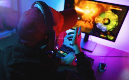 Photo for Professional Gamer pointing and Playing in First-Person Shooter Online Video Game on His Personal Computer. Room Lit by Neon Lights in Retro Arcade Style. Online Cyber e-Sport Internet Championship - Royalty Free Image