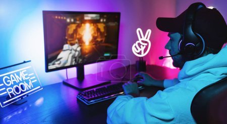 Jugador jugando en primera persona Shooter Juego de vídeo en línea en su potente ordenador personal. La habitación y la PC tienen luces led de neón coloridas. Hombre joven está jugando con una gorra en casa