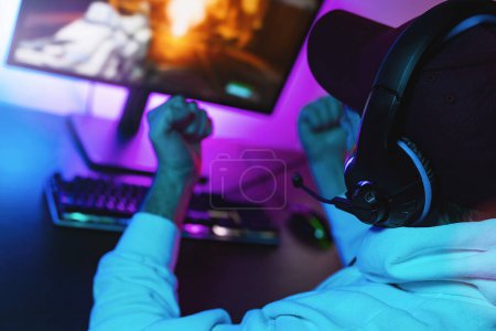 Photo for Gamer is happy abou Playing and Winning in First-Person Shooter Online Video Game on His Personal Computer. Room Lit by Neon Lights in Retro Arcade Style. - Royalty Free Image