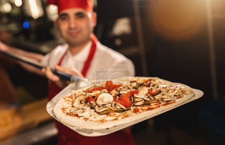 Foto de Panadero de pizza italiana sosteniendo pizza fresca en la cáscara en la pizzería - Imagen libre de derechos