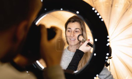 Téléchargez les photos : Mannequins visage posant à la caméra à travers la lampe à lumière annulaire à la séance photo et maquilleur - en image libre de droit