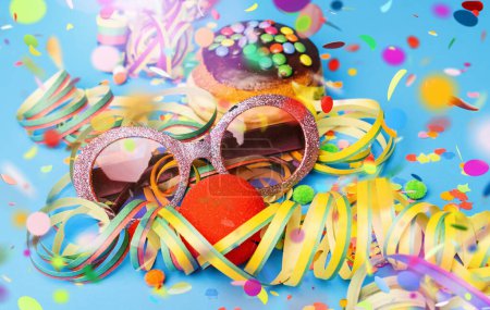 Karnevalssonnenbrille mit Donut aus Deutschland mit Puderschokoladenzucker auf blauer Fläche mit Konfetti und Luftschlangen darauf - Hintergrund für eine Karnevalsparty oder Partys