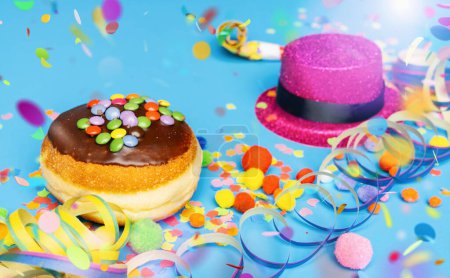 Téléchargez les photos : Donut de carnaval d'Allemagne avec du sucre glace au chocolat sur une surface bleue avec des confettis et des banderoles dessus - fond pour une ou plusieurs fêtes de carnaval - en image libre de droit