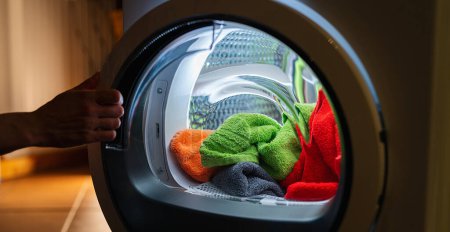Foto de Ama de casa abre una lavadora o secadora por la noche con muchas toallas limpias y coloridas - Imagen libre de derechos