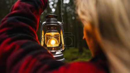 Foto de Mujer excursionista sosteniendo una lámpara de queroseno o una linterna de aceite en el bosque oscuro - Imagen libre de derechos