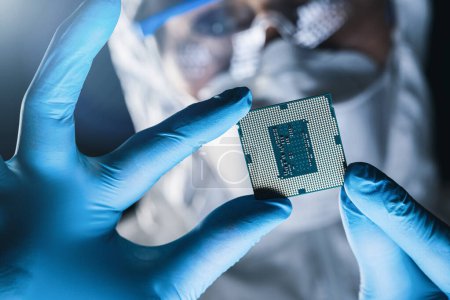 in hochmoderner elektronischer Fertigung Konstrukteur im sterilen Overall hält Mikrochip mit Handschuhen und untersucht ihn