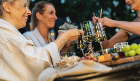 Freunde genießen Wein und Essen im Freien in der Nähe einer finnischen mobilen Sauna in der Abenddämmerung