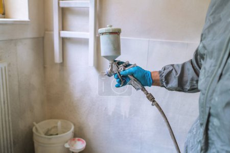 Worker using a spray gun to paint, wearing safety gloves and protective clothing
