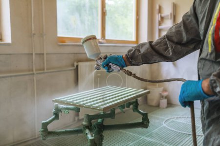 Person in a protective suit spray painting a wooden panel in a carpentry workshop