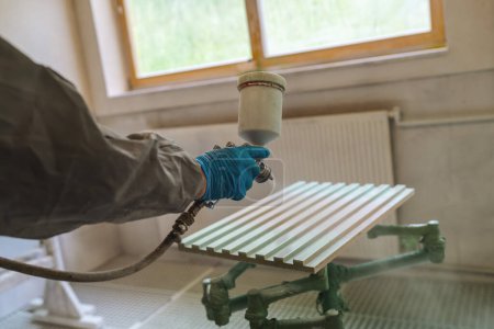 Person in protective clothing spray painting a bench with a window in the background