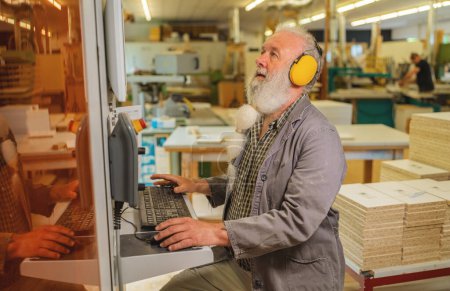 Man using computer on a cutting machine in a woodworking workshop