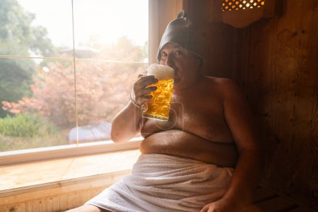 Foto de Hombre en una sauna finlandesa con un sombrero de fieltro, bebiendo una taza de cerveza alemana, con una ventana brillante en el fondo. Oktoberfest concepto de imagen - Imagen libre de derechos