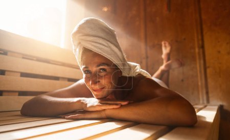 Foto de Mujer relajándose en una sauna finlandesa, con una toalla en la cabeza, sonriendo a la cámara - Imagen libre de derechos