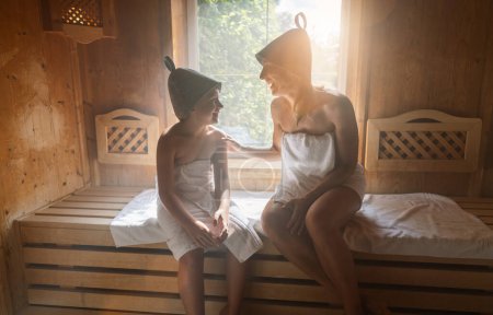 Mother and daughter enjoying a sauna session, wearing felt hats and wrapped in towels