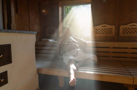 Man sitting in a sauna with light streaming through the window onto his relaxed figure.