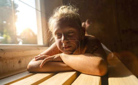 Niño descansando en un banco de sauna, la luz del sol filtrándose a través de una ventana, los ojos cerrados
