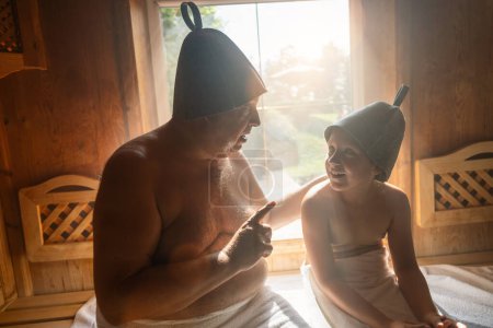 Padre e hija en sauna finlandesa, usando sombreros de fieltro, padre hablando e hija escuchando.