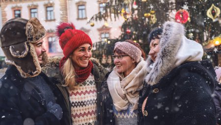 Téléchargez les photos : Amis riant ensemble à un marché de Noël enneigé - en image libre de droit