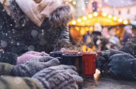 Photo for Hands in gloves around steaming mugs of mulled wine at a christmas market, with copyspace for your individual text. - Royalty Free Image