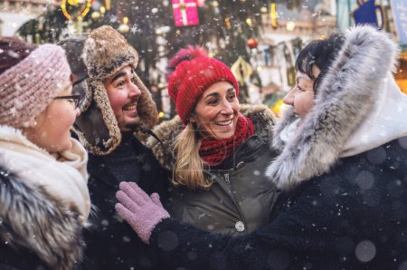 Téléchargez les photos : Groupe d'amis partageant des moments joyeux dans un marché de Noël enneigé - en image libre de droit