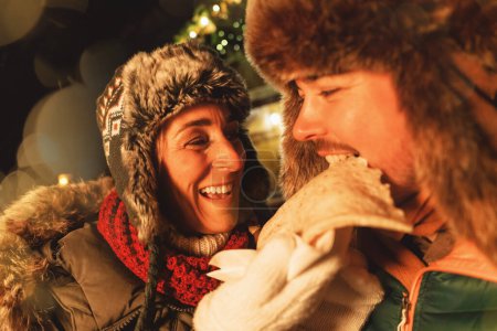 Pareja disfrutando de un crepé juntos en un mercado de Navidad, compartiendo alegremente el momento