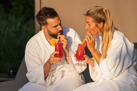 Mann und Frau in weißen Gewändern schlürfen Cocktails in goldenem Stundenlicht im Kurhotel Resort