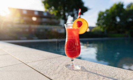 Erfrischender roter Cocktail, garniert mit einer Erdbeer-Orangen-Scheibe am Pool bei Sonnenuntergang