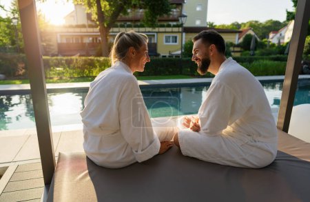 Paar in weißen Bademänteln genießt Sonnenuntergang am Pool eines Wellnesshotels