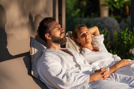 Entspanntes Paar in weißen Bademänteln faulenzt draußen im Sonnenlicht