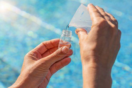 Servicetechniker gießt vor Pool-Hintergrund Wasser in Testfläschchen für PH-Wert-Test