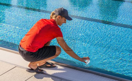 Lifeguard crouching by swimming pool collecting water sample in a clear container in a hotel