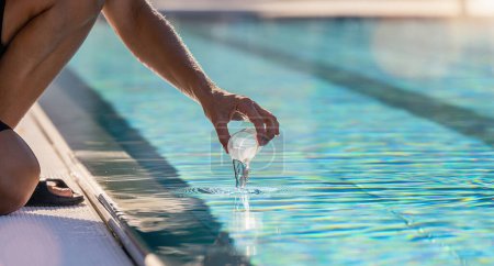Persona que recoge una muestra de agua de una piscina con una pequeña taza transparente