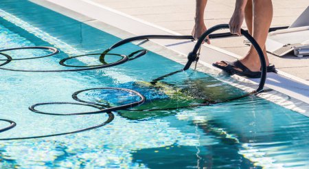 Persona que usa una manguera de un robot limpiador de piscinas en el borde de una piscina