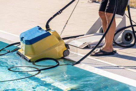 Pool cleaning robot being placed by a person next to a swimming pool