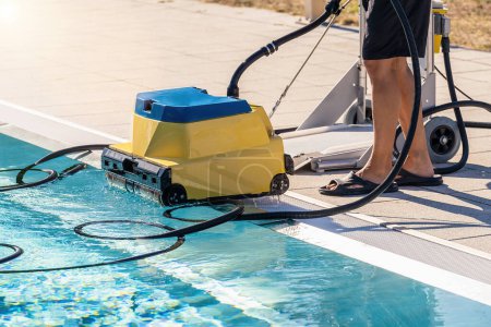 Automated pool cleaning robot being used by person at the edge of a pool