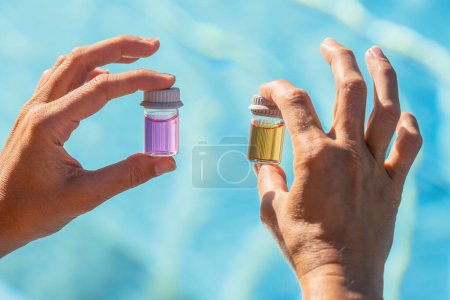 Manos sosteniendo viales con líquidos rosados y amarillos para la prueba de pH del agua de la piscina en un balneario de bienestar del hotel