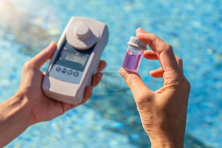 Person testet Schwimmbadwasser mit digitalem Testgerät und kleinem Probengefäß