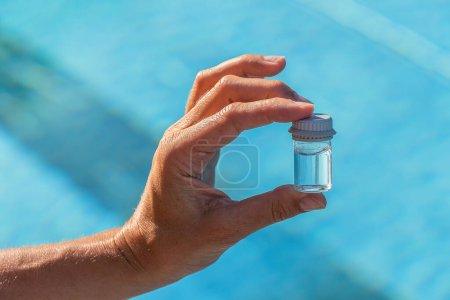 Técnico de la piscina Manos sosteniendo un vial de agua para pruebas de pH cerca de una piscina en un hotel spa