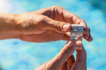 Nahaufnahme Hände, die ein Fläschchen Wasser für pH-Tests in der Nähe eines Swimmingpools in einem Hotel verschließen