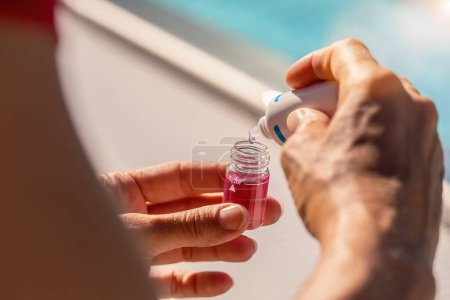 Manos de un técnico de la piscina que dispensa el disolvente de la botella del gotero en un vial con la solución rosada para la prueba del pH