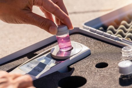 Colocación manual de una botella de líquido rosa en un dispositivo de análisis digital en un kit de prueba