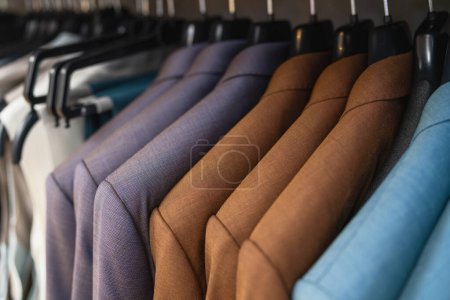 Row of suits on hangers, varying shades of brown and blue, formal wear display at a store